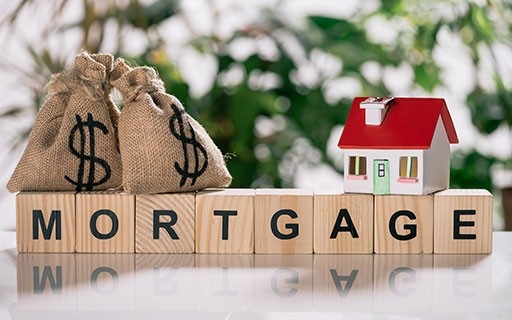The word "mortgage" spelled out on wooden blocks with a model house and bags of money on top of it.