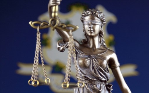A bronze statue of Themis, Greek goddess of law and justice, in front of the Connecticut flag.