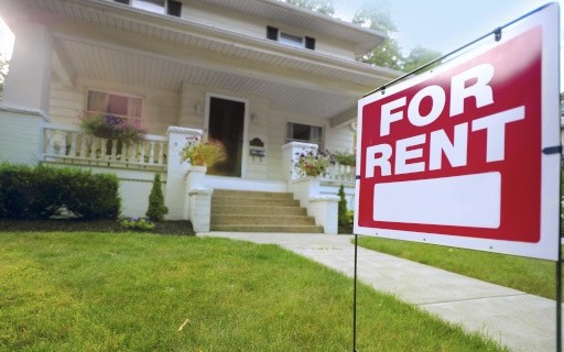 A red "For Rent" sign in the yard in front of a charming bungalow.