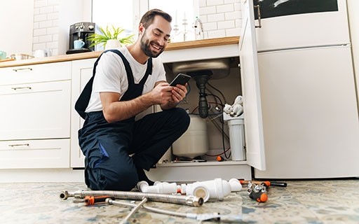 Man checking maintenance requests on his phone as he fixes a sink.