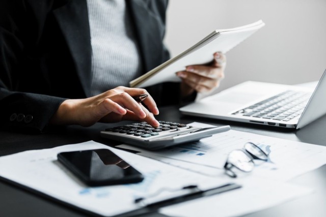 A person holding a notebook and using a calculator
