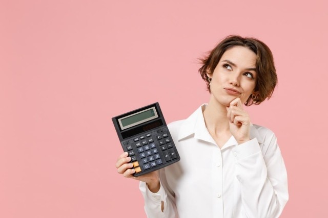 A lady is holding a calculator with an inquisitive look on her face