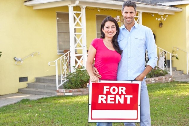 A couple standing in front of a for rent sign at a home