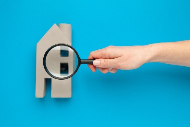 A hand holding a magnifying glass over a miniature house