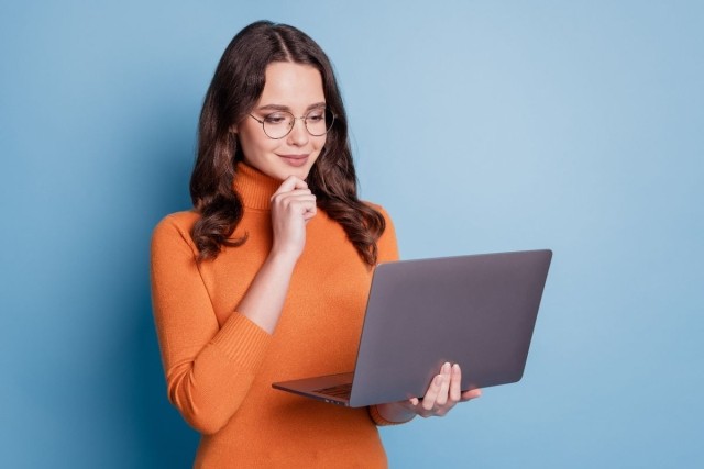 A professionally dressed woman smiling and looking at her laptop screen.