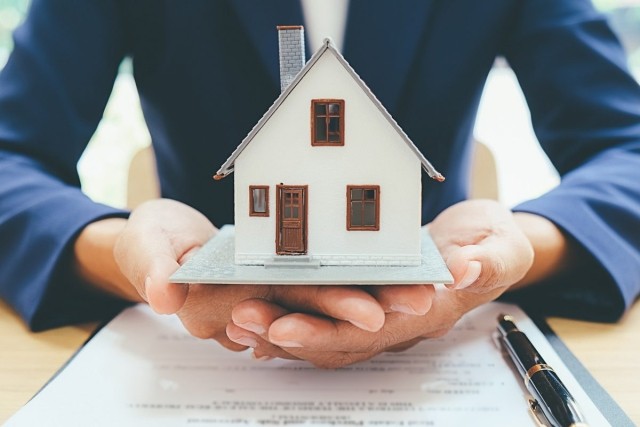 A businessman holding a small model house in his hands, depicting overseeing a property with care.